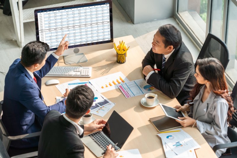 Several professionals in an office environment, reviewing data and graphs on a computer screen and paper documents